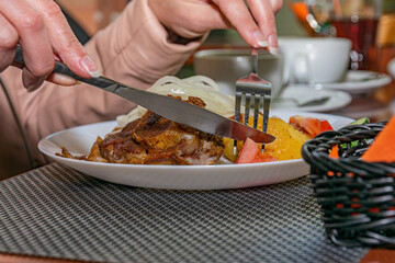A woman eats a hot meat dish in a restaurant. Lamb kabob with fresh vegetables and fried potatoes.