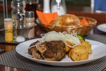 POV Lamb cauldron kabob with fresh vegetables and fried potato on white plate.