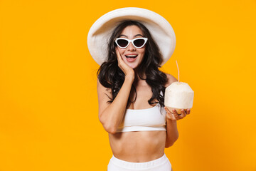 Image of woman in swimsuit and hat smiling and holding coconut