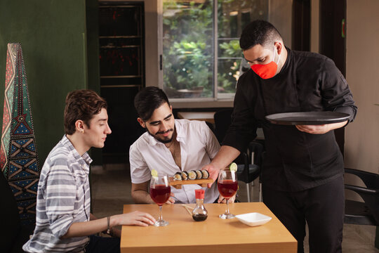Waiter With Biosecurity Measures In Times Of Coronavirus. Person Serving Sushi In A Reopened Restaurant