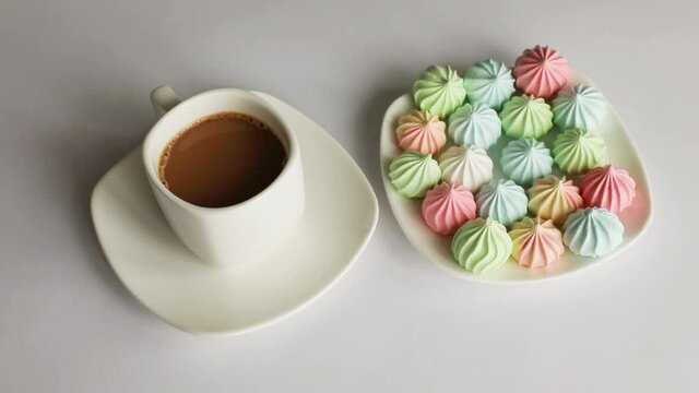 Multicolored meringuesand a cup of coffee on a white background