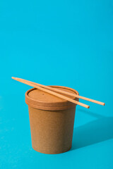 Craft takeaway food container with chopsticks on a blue background. Delivery food.