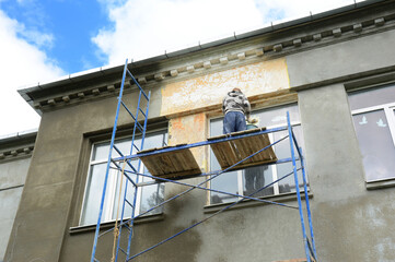 A building contractor high on scaffolding near the roof is plastering, lime rendering, coating the...