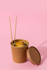 Vegetable broth with green beans, egg and sesame seeds in a craft container on a pink background. Food Delivery Concept.