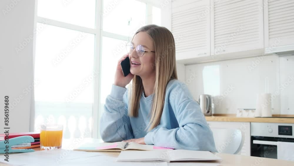 Poster a pleased young blonde woman wearing glasses is talking on her smartphone while working in the white