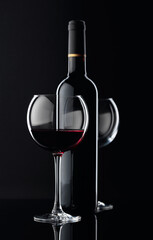 Bottle and glasses of red wine on a black background.