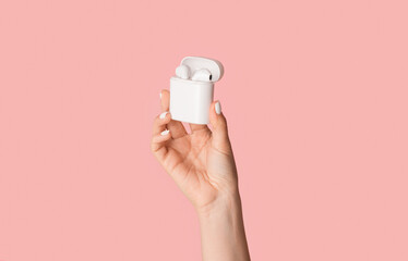 Cropped view of millennial girl holding modern earbuds in box on pink background