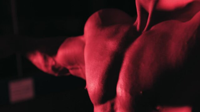 posing muscular bodybuilder in red light with a dark background