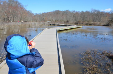 child in blue jacket using binoculars with boardwalk in wetland