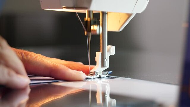 Sewing machine needle stitching cotton fabric in slow motion. Woman hand sewing cloth face mask.