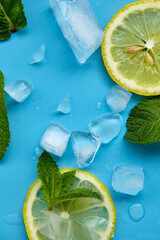 Composition with cut citrus fruits on blue background. Creative summer background composition with lemon slices, leaves mint and ice cubes. Minimal top down lemonade drink concept.Top view