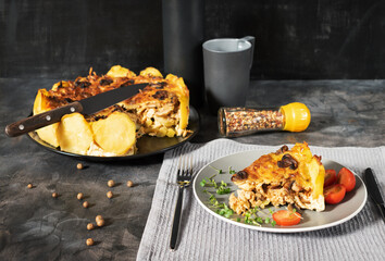 Homemade Lorraine pie with potatoes, chicken, mushrooms, cheese, onions and seasonings. In a gray plate, on a dark table with cherry tomatoes, a gray napkin, microgreens and spices.