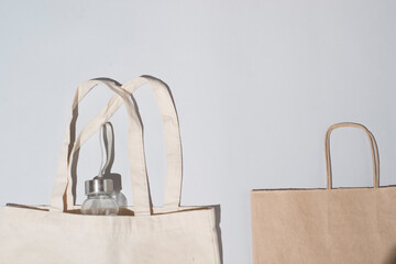 Zero waste shopping concept - cotton bag, craft paper bag, glass bottle for water, hard light, on a light background.