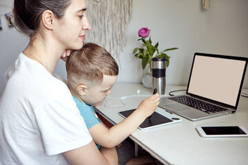 A woman with a child works at a computer. Concept of work from home and home family education. Mom and son are is working on a graphics tablet and on a laptop at home.