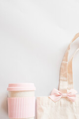 Zero waste shopping concept - cotton bag with pink bow, reusable cup for tea coffe with spring flowers, herbs and leaves on a light background.