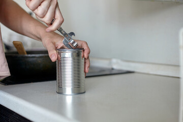 A woman in the kitchen opens a can. Hand open canned food in metal can. Close up canned goods non...