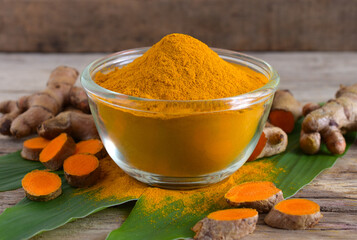Turmeric (curcumin) powder in a glass bowl  and root on wooden background.