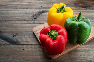 red, green and yellow sweet bell peppers on wood background, paprika, organic vegetables
