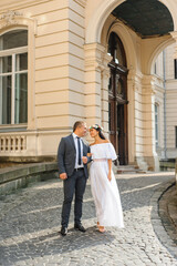 Wedding photo session on the background of the old building. The bride and groom are smiling at each other. A woman holds a man's hand. Rustic or Boho Style Wedding Photography