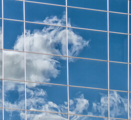 the clouds are reflected on the glass of a large office building