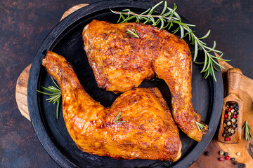 Baked chicken legs in a ceramic black baking dish on a wooden kitchen board.