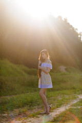 Portrait of a young beautiful girl in a sundress. Summer photo session in the park at sunset. The bright sun shines in the frame.