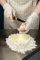 The cook breaks the egg into a mixture of flour and butter on kitchen table from stainless steel.