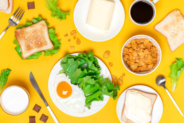 Breakfast on a yellow background top view. Fried eggs, lettuce, toast, cereal, milk and coffee on a yellow background, flat lay. Different breakfast options. Food background.