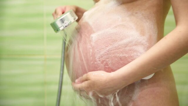pregnant woman in the shower lathers a big belly under water