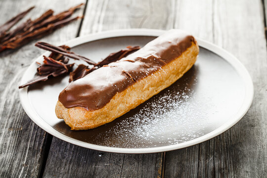 Tasty eclair with chocolate cream on plate standing on old wooden table