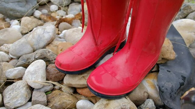 Close-up of low section of 4 years old child girl with red rubber boots standing on stones and kneeling down. Seen in Germany in June.