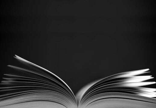 Open book (color) with narrow depth of field on black background. Black and White photo, space for text above the book