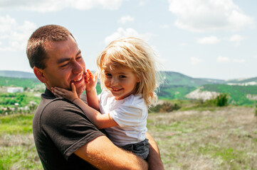 Fototapeta premium Joyful dad and daughter are playing outdoors in the park. The concept of a happy family. Dad with a baby.