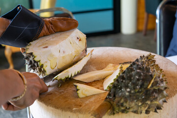 Durian Seller are showing how to open and explain informations and details to audiences about type of durain on the lunch table.