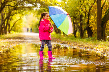 Adorable toddler girl with colorful umbrella outdoors at autumn rainy day