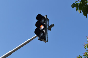 Ampel steht auf "Gelb", vor blauem Himmel mit Bl&auml;ttern einer fr&uuml;hlingshaften Kastanie	
