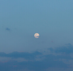 Big beautiful full moon in the blue cloudy evening sky with a cloud intersecting the supermoon in...