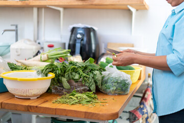 Asian female is holding knife and preparing a lot of vegetable for the cooking in backside kitchen.