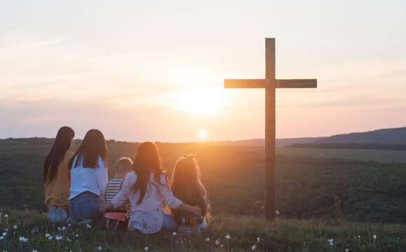 Christian family. Happy family on the nature. Wooden cross against the sky. Cross. Crucifixion on the background of the sky and sunset. Easter. Calvary.