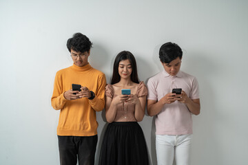 group of young asian friends with serious expressions while using their smart phones while standing against an isolated background