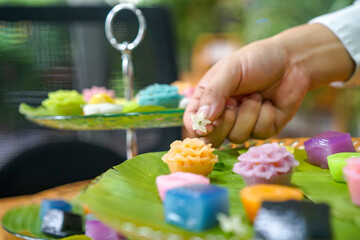 Obraz na płótnie Canvas Thai Chef's hand is decorating Varieties traditional colorful Thai desserts set; steaming flour, black custard, coconut custard & steaming bean, layer pudding cake