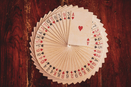 Deck of playing cards arranged in circular stack or design or pattern with ace of hearts on top on a wooden background for performing illusion or magic trick. Poker playing cards. Casino. Magician.