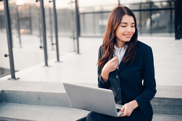 Successful smiling businesswoman or entrepreneur using laptop sitting in front of his office.