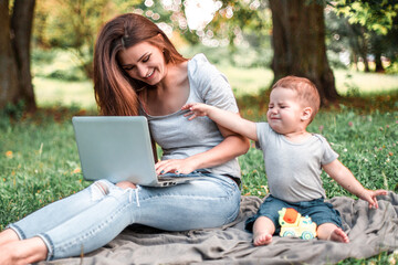 Mother with son sitting in the park and work on laptop.