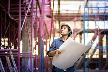 Female Engineering checking on the scaffolding. Forewoman inspect construction site. Engineering woman holding blueprint looking drawing layout. Woman wearing safety helmet going through site.