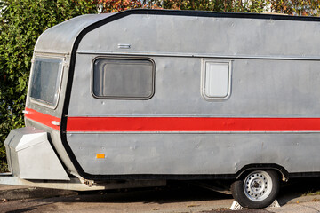 Small grey, red retro camping trailer from the 1980's, parked near a sidewalk in a small German village