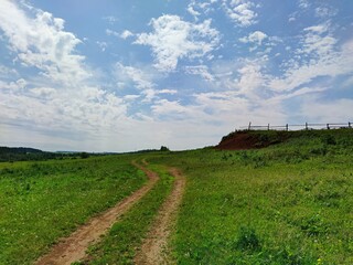 winding country road in a field near a farm paddock against a beautiful blue sky with clouds on a sunny day