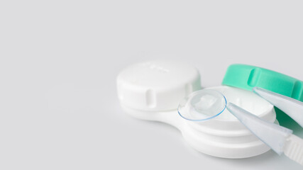 White container case for contact lenses, tweezers on a light gray background close-up. The concept of poor vision, hyperopia, myopia