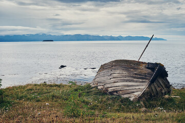 Old wooden boat abandoned on the shore of the fjord. North of Iceland.