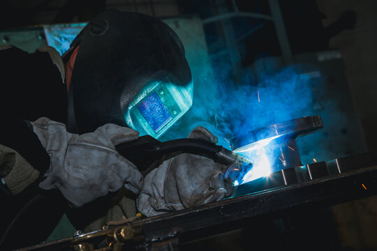 Close-up blacksmith welder in protective mask works with metal steel and iron using a welding machine, bright sparks and flashes. Welder uses a mask to protect your eyes from sparks. © spocktv